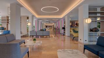 A modern hotel lobby with a marble floor, seating areas, and a reception desk.