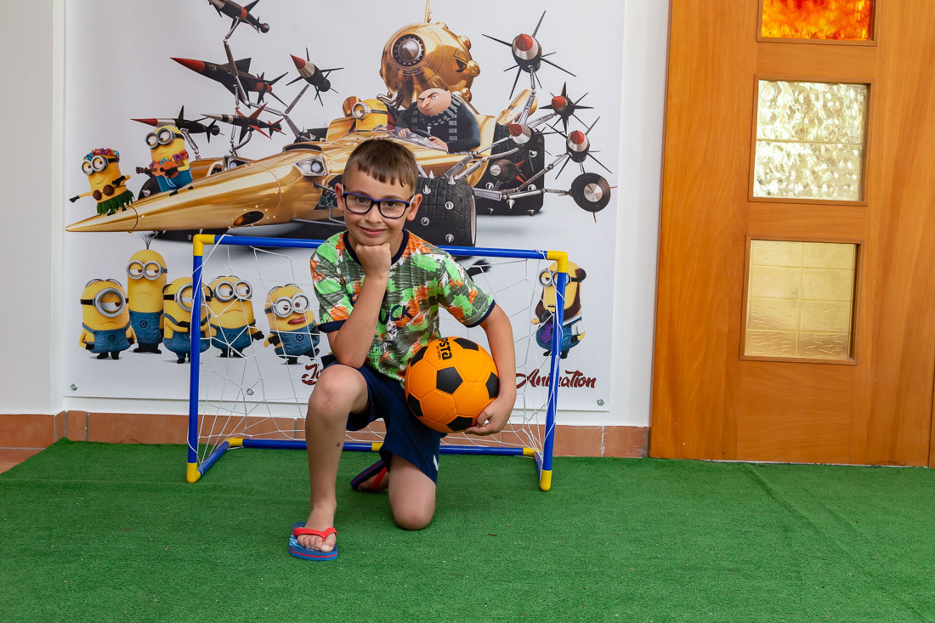 A child with a soccer ball in front of a wall with a Minions-themed mural.