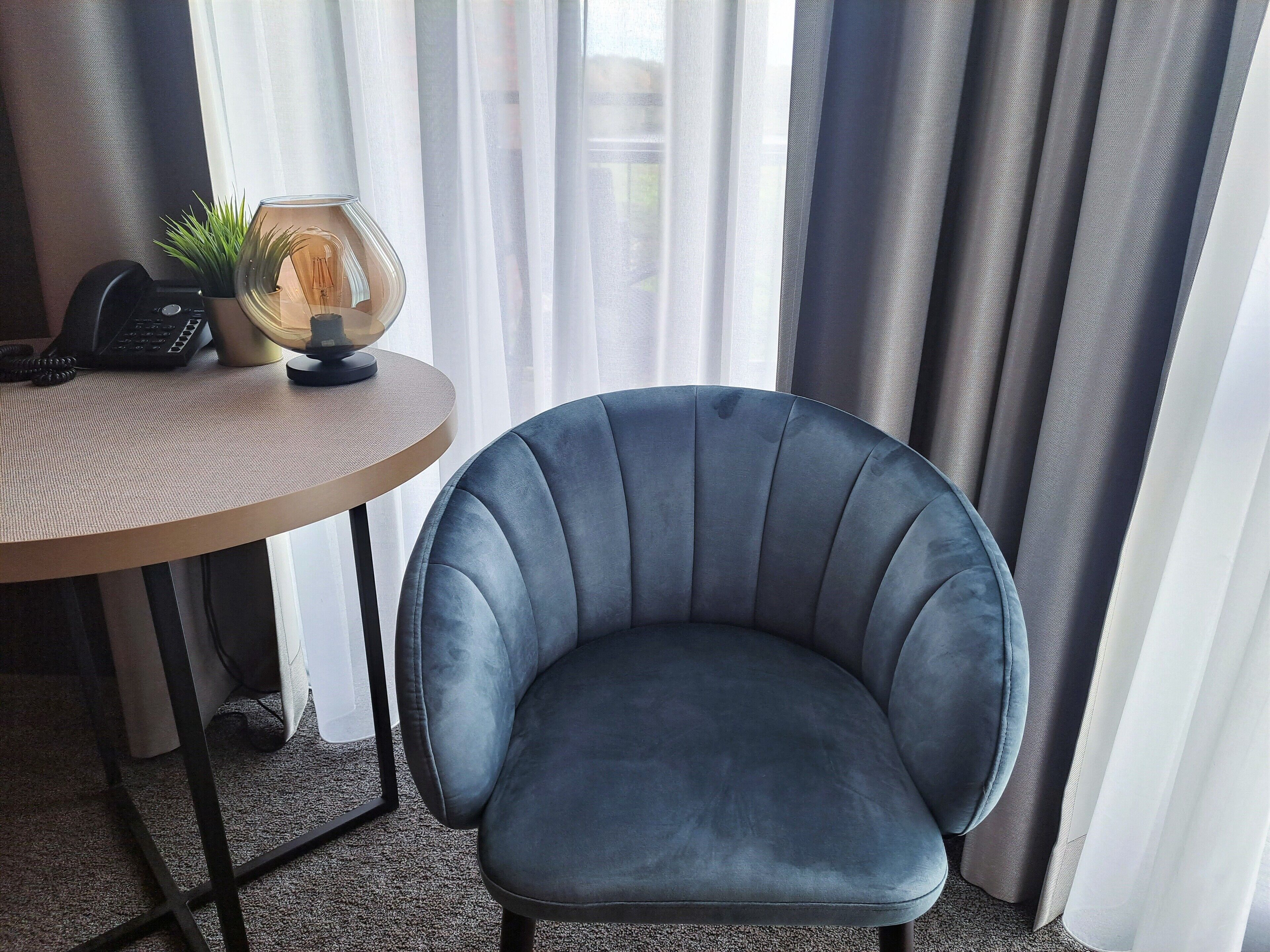 A room with a round table, a blue armchair, a telephone, and a small plant.