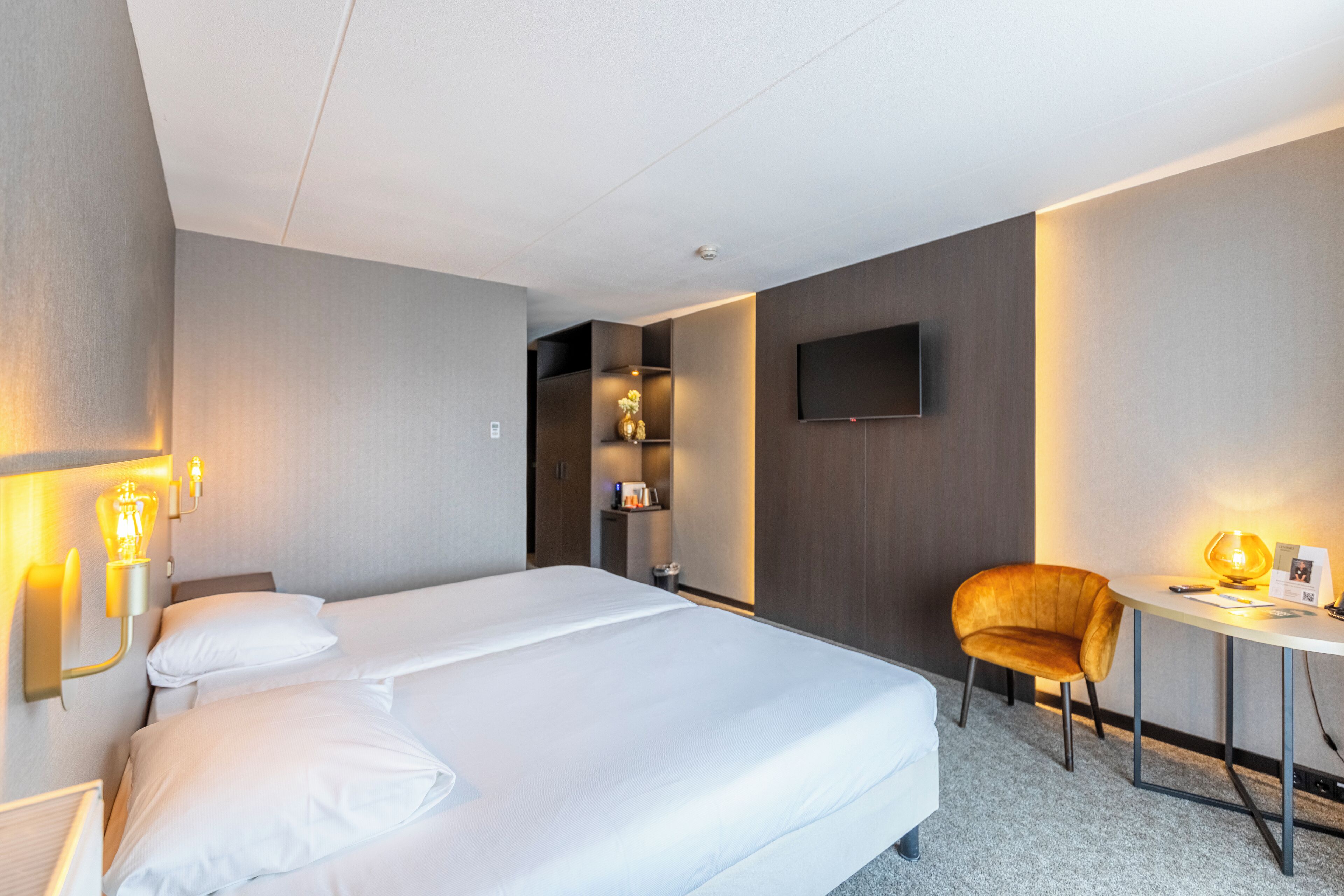 Habitación de hotel con cama, mesitas de noche, escritorio, silla, televisor de pantalla plana y estante con objetos decorativos.