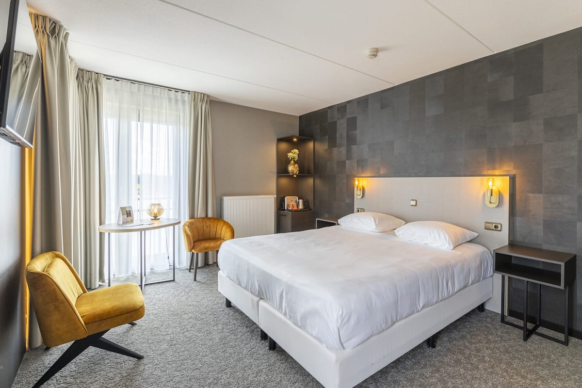 A modern hotel room with a large bed, a small table, a chair, and a decorative vase.