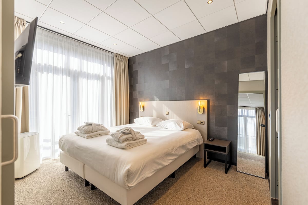 A modern hotel room with a large bed, bedside lamps, a small table, and a mirror.