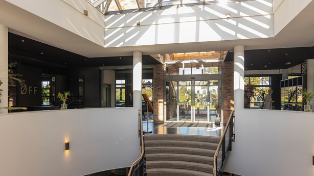 Un interior moderno con una escalera central, puertas de cristal que dan al exterior y un tragaluz arriba.