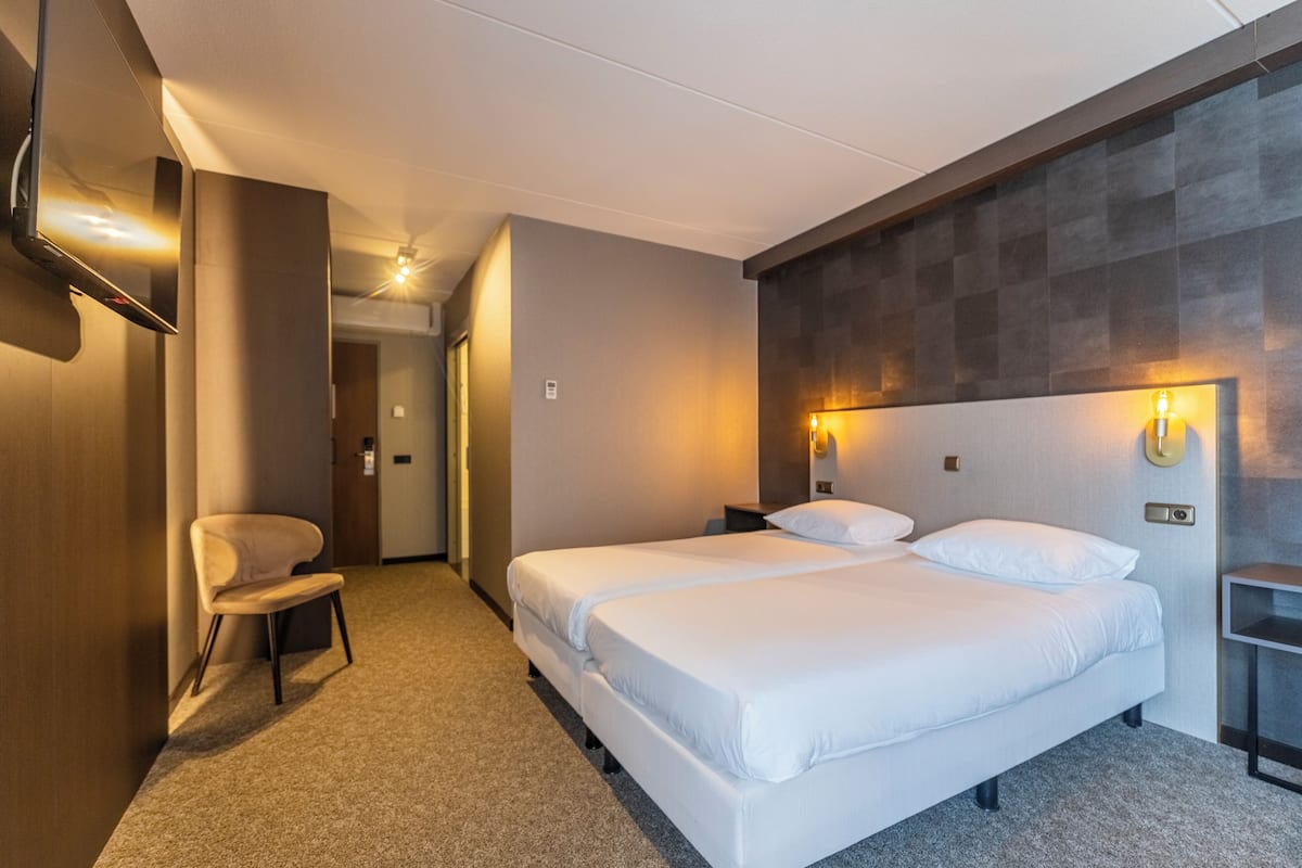 A hotel room with a double bed, a chair, a TV mounted on the wall, and a small table.