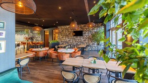 Un restaurante con mesas redondas, sillas anaranjadas y lámparas de mimbre colgantes.