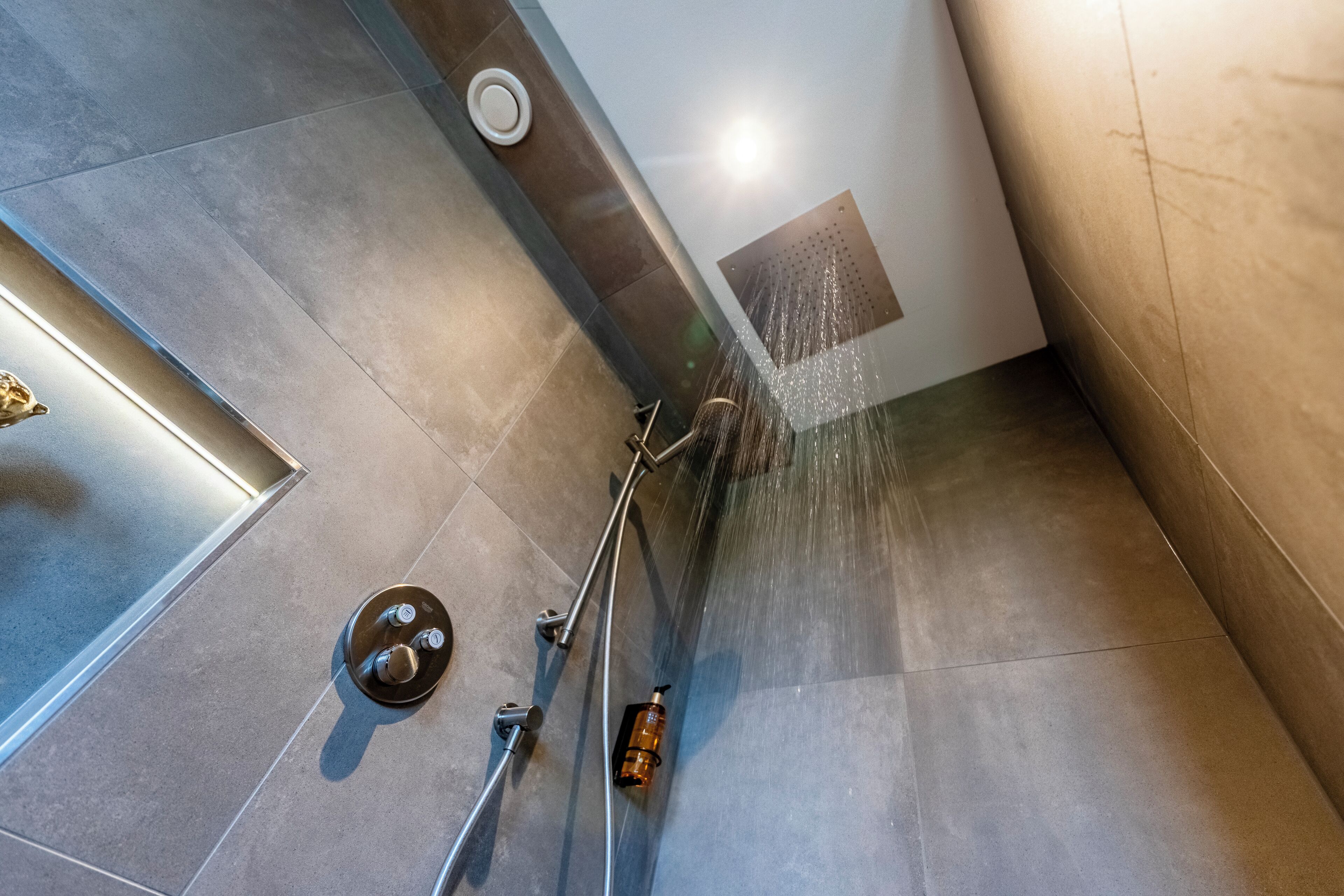 A modern shower with a handheld showerhead and a wall-mounted control panel.