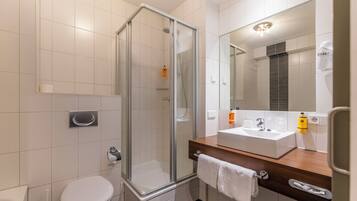 Een moderne badkamer met een douchecabine van glas, een wit toilet en een houten wastafelmeubel met een wastafel en spiegel.