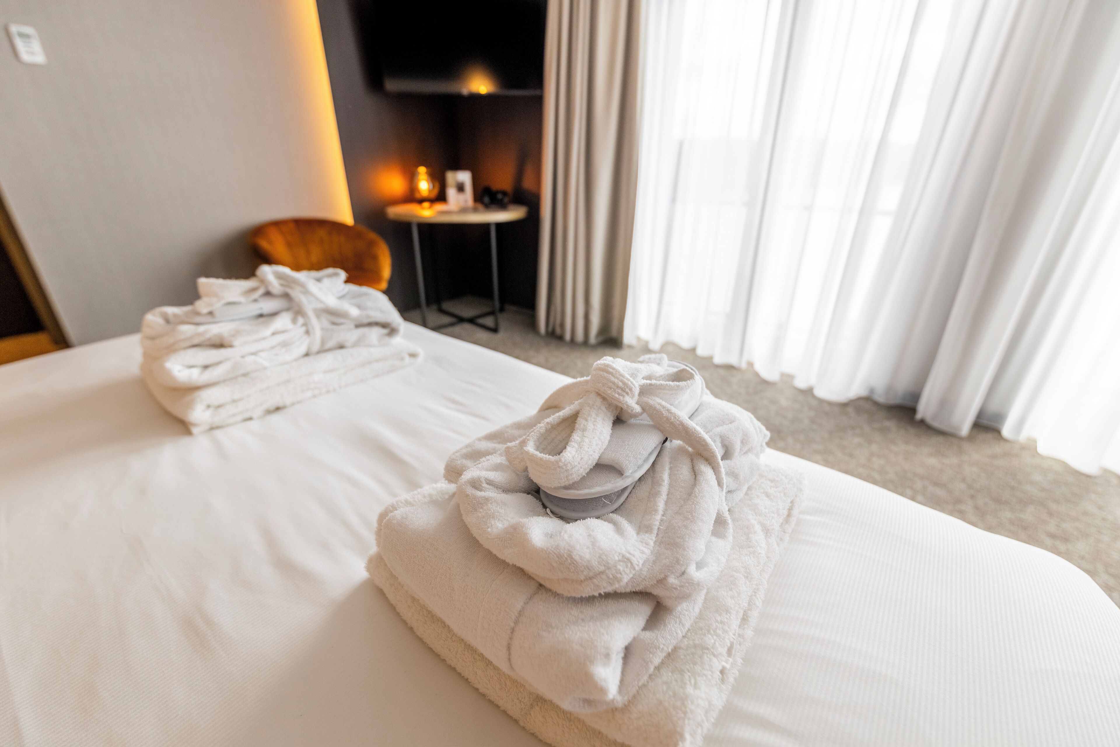 A hotel room with two beds, a small table with a lamp, and a TV on the wall.