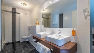 Un bagno moderno con due lavandini, uno specchio grande e una zona doccia.