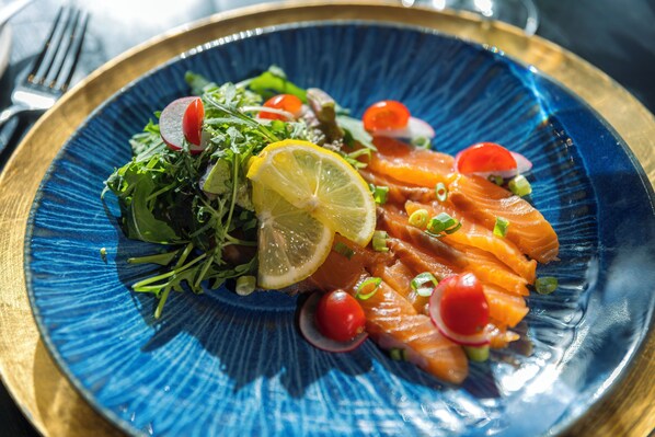 A blue plate with salmon, lemon, and cherry tomatoes.