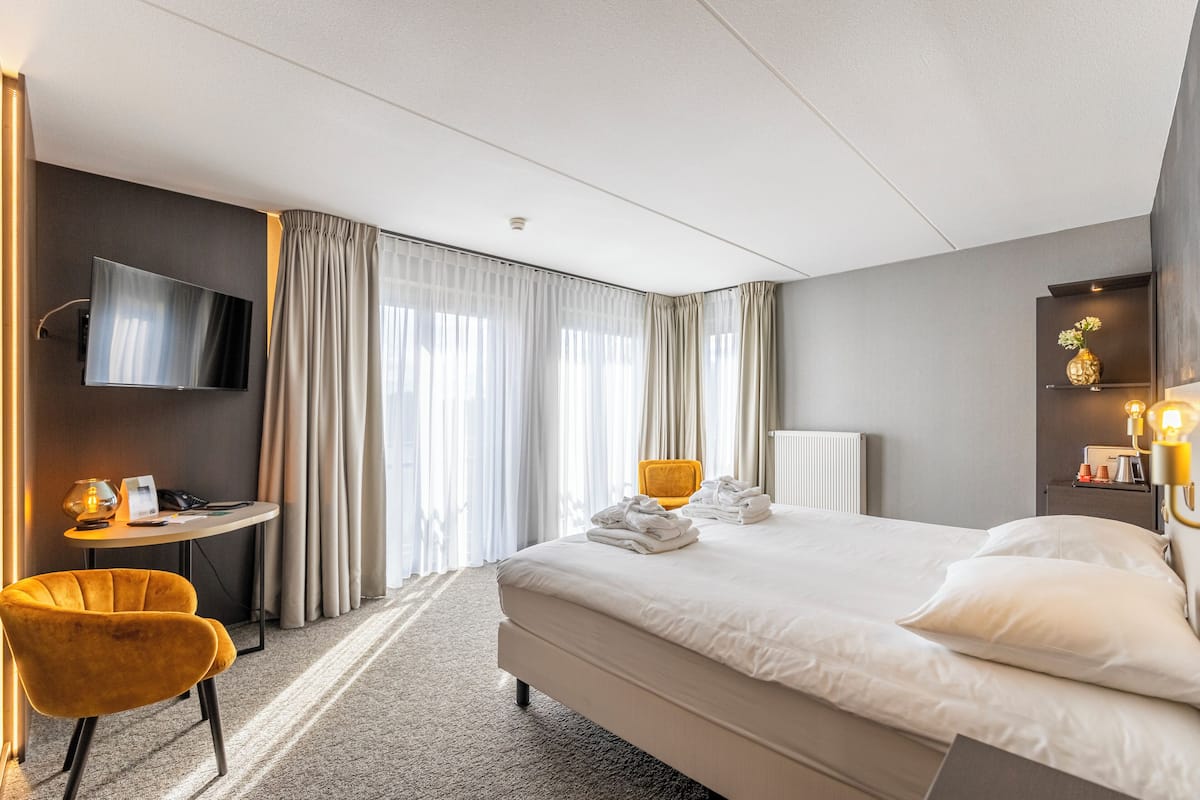 A hotel room with a bed, a desk, a chair, a TV, and a lamp.