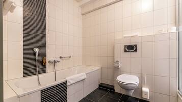 A modern bathroom with a bathtub, toilet, and a large mirror.