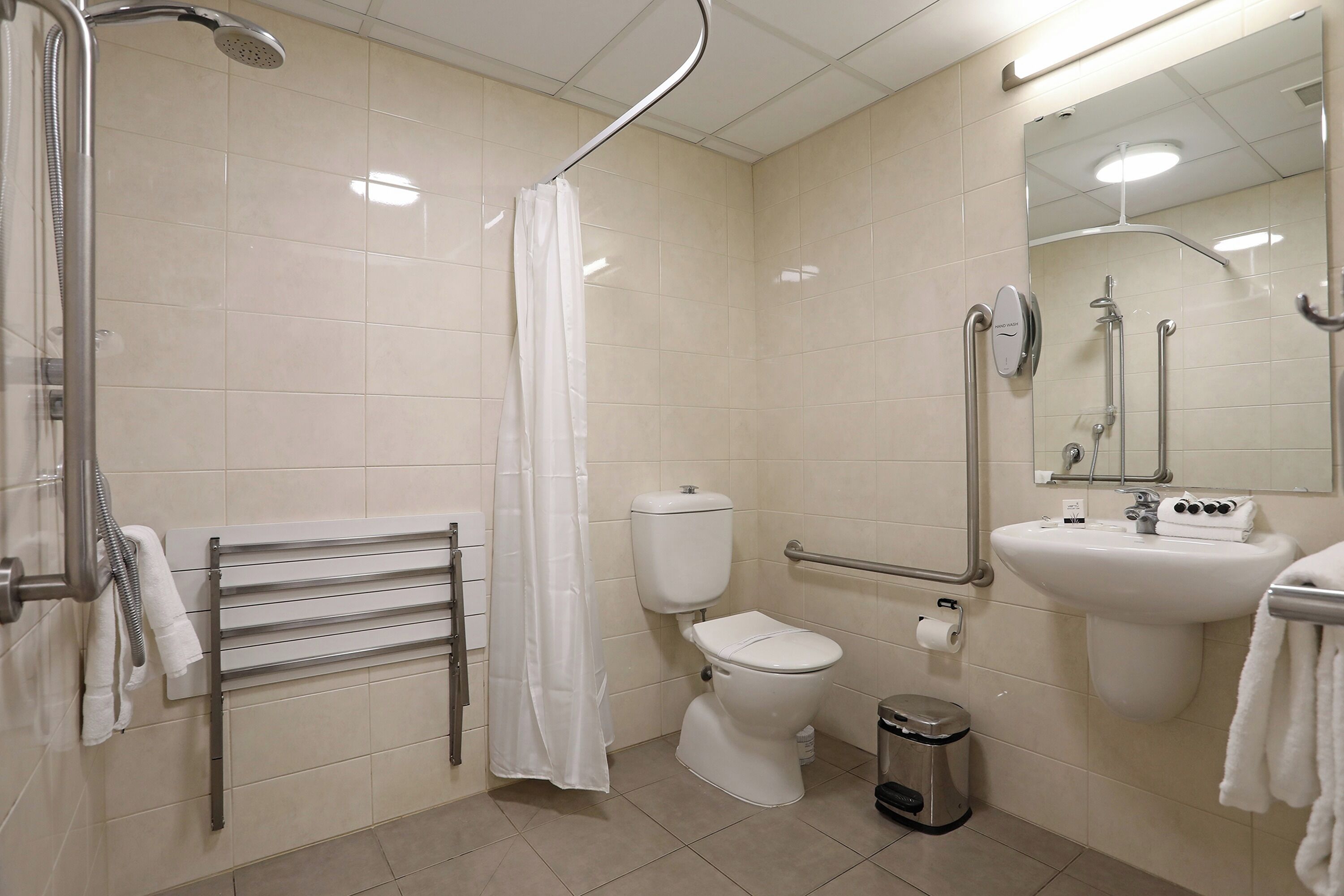 Baño con ducha, inodoro, lavabo y barras de apoyo.