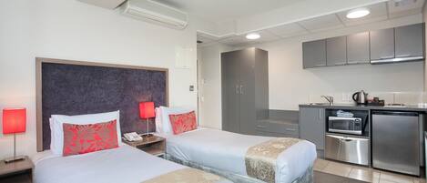 A hotel room with two beds, a kitchenette, and a bathroom.