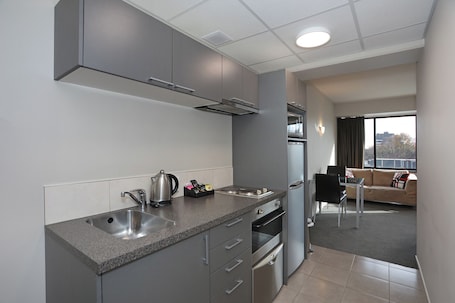 A modern kitchen with a granite countertop, stainless steel appliances, and a view to a living area with a sofa and a dining table.. Ramada Encore By Wyndham Palmerston North