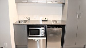 A compact kitchen with stainless steel appliances, including a microwave and dishwasher, and grey cabinetry. - Ramada Encore By Wyndham Palmerston North (Palmerston North)
