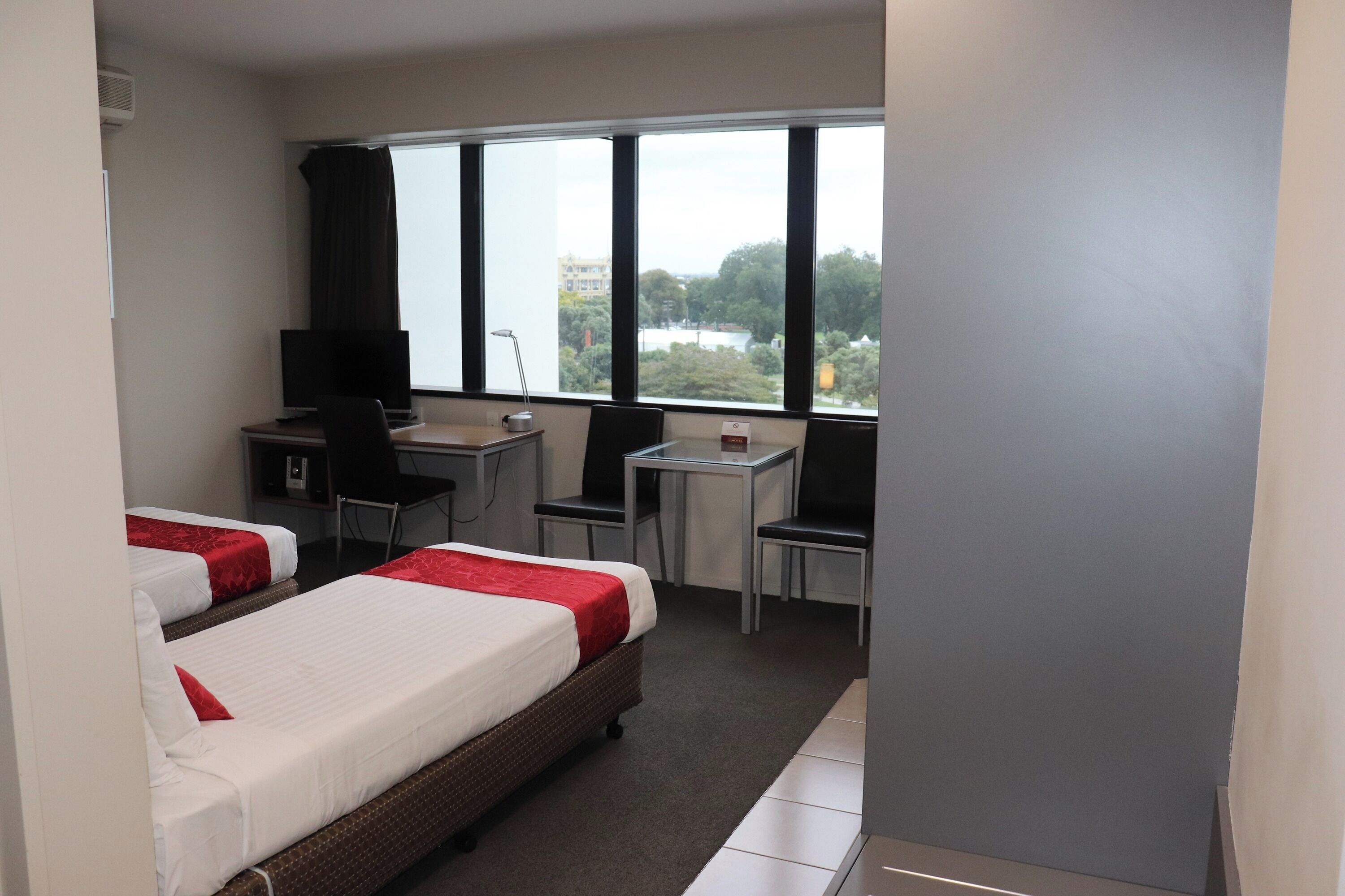 A hotel room with two beds, a desk, a chair, and a window with a view.