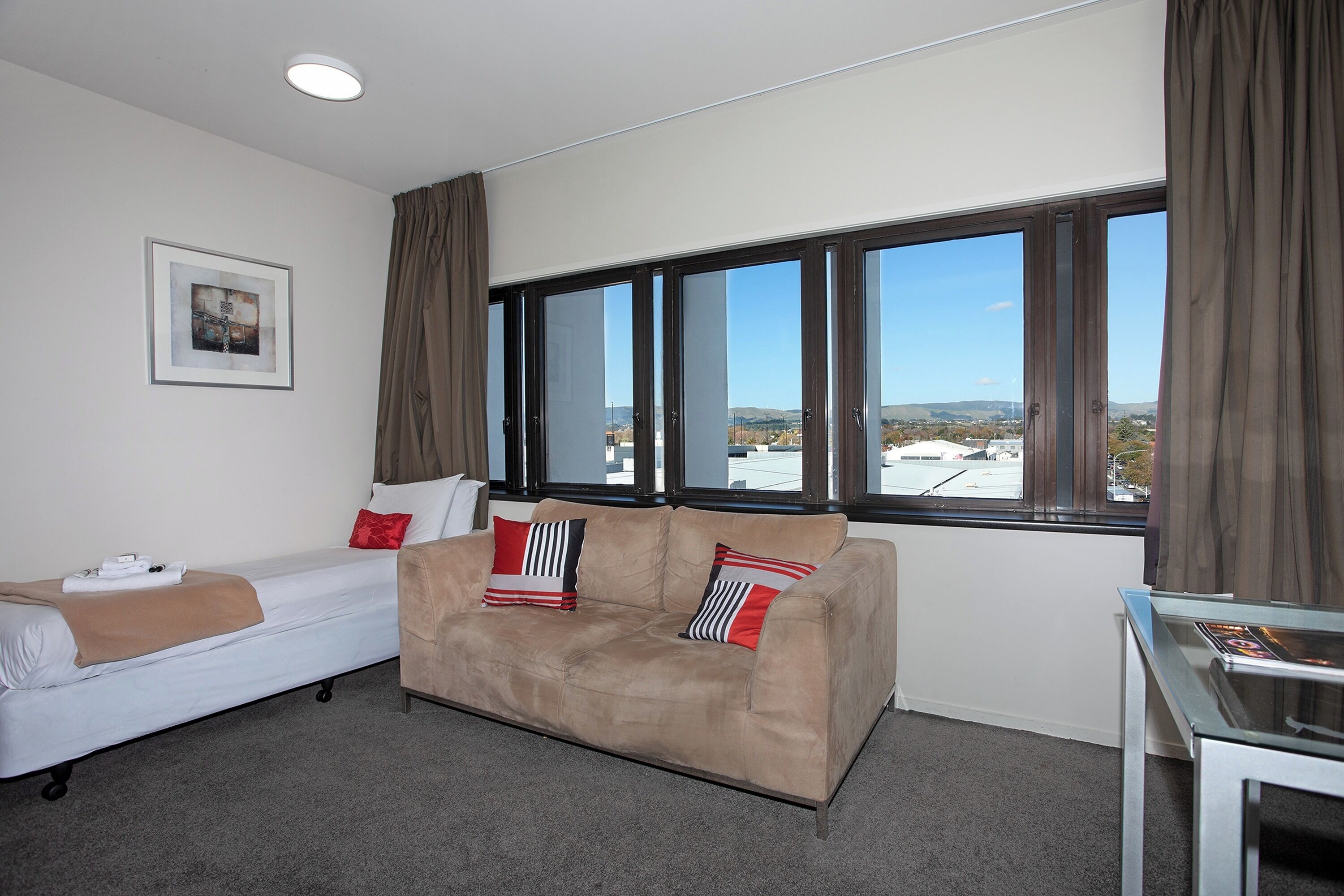 A hotel room with a bed, a sofa, a window with curtains, and a framed picture on the wall.