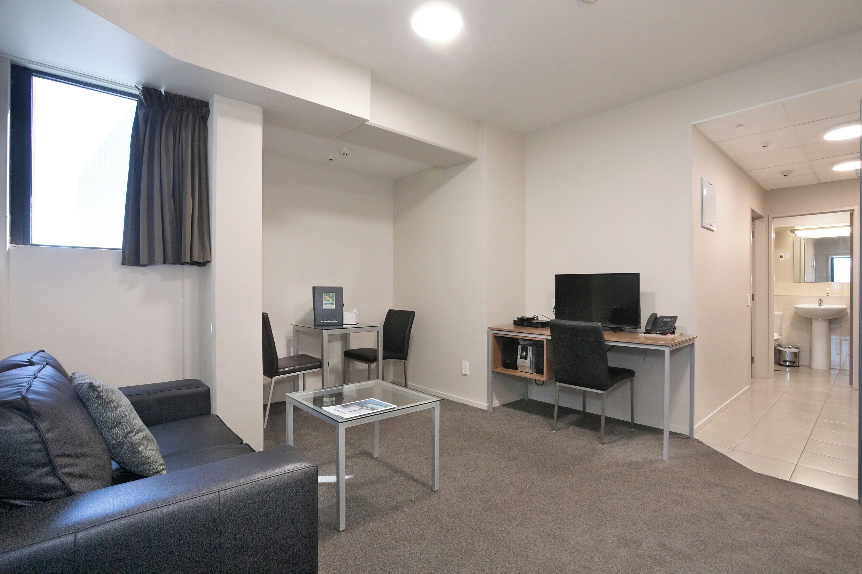 A modern office space with a desk, computer, chairs, a glass coffee table, and a sofa.