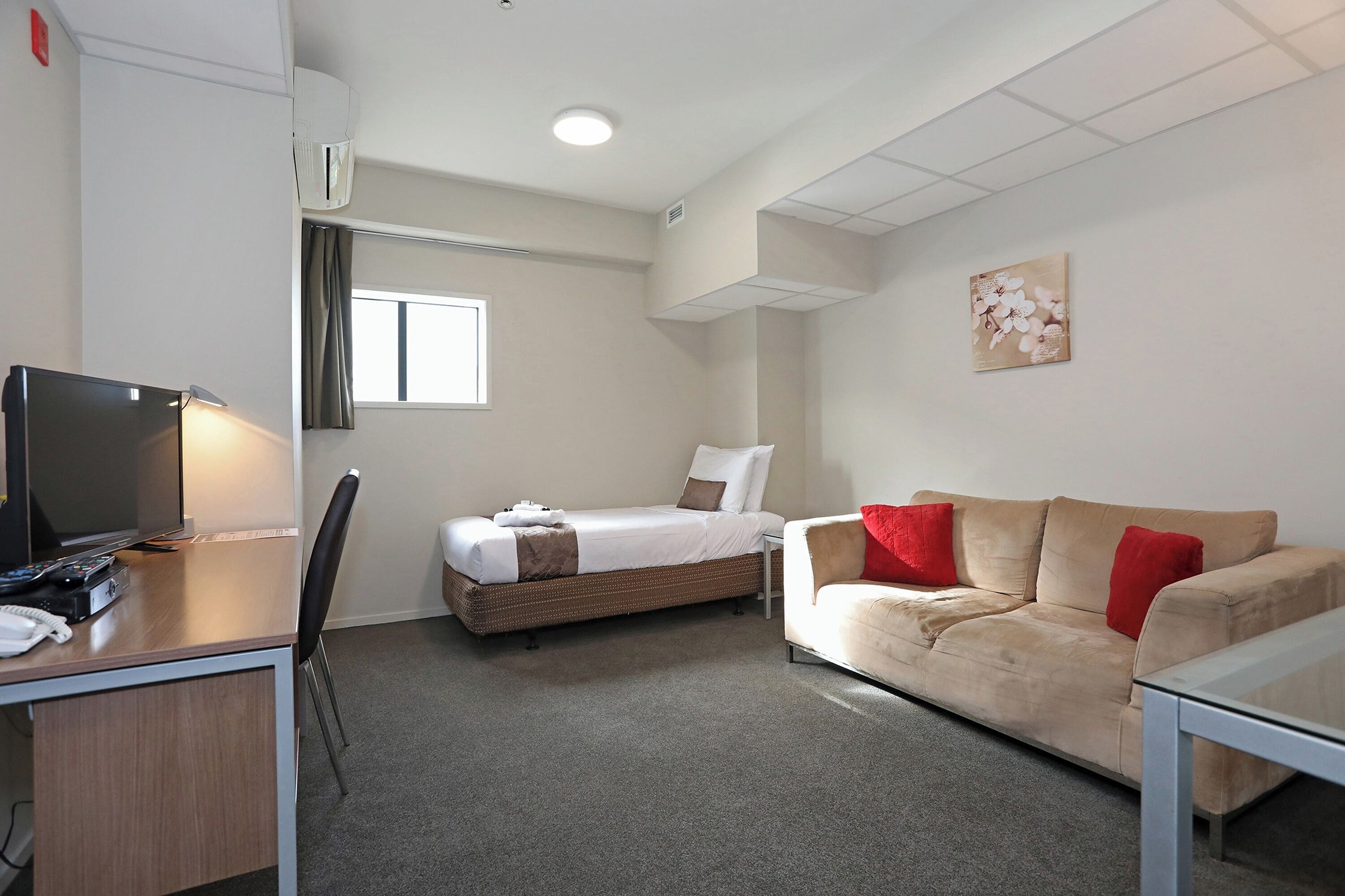 Ein Hotelzimmer mit einem Bett, einer Couch, einem Schreibtisch mit Fernseher und einem Fenster.