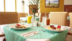 A dining table with two plates of breakfast, a vase with a plant, and a glass of orange juice. - Hotel Mision Santa Maria (San Quintin)
