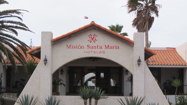 The entrance to Mission Santa Maria Hotels with a tiled roof, arched doorway, and surrounding palm trees. - Hotel Mision Santa Maria (San Quintin)