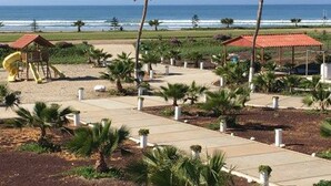 A beachside park with a playground, palm trees, and a view of the ocean. - Hotel Mision Santa Maria (San Quintin)