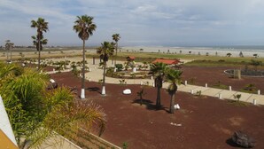 A landscaped area with palm trees, a red-roofed structure, and a view of the beach. - Hotel Mision Santa Maria (San Quintin)