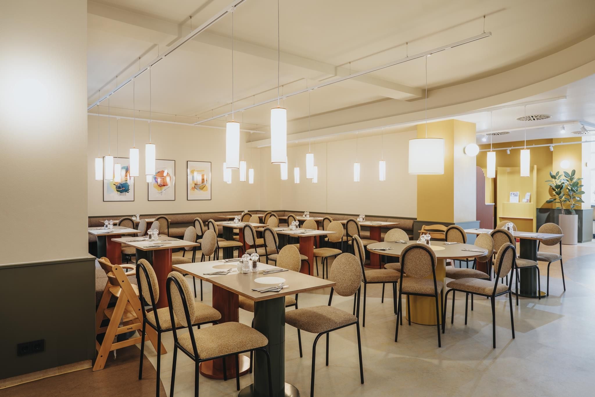 A spacious dining area with multiple tables and chairs, pendant lighting, and artwork on the walls.