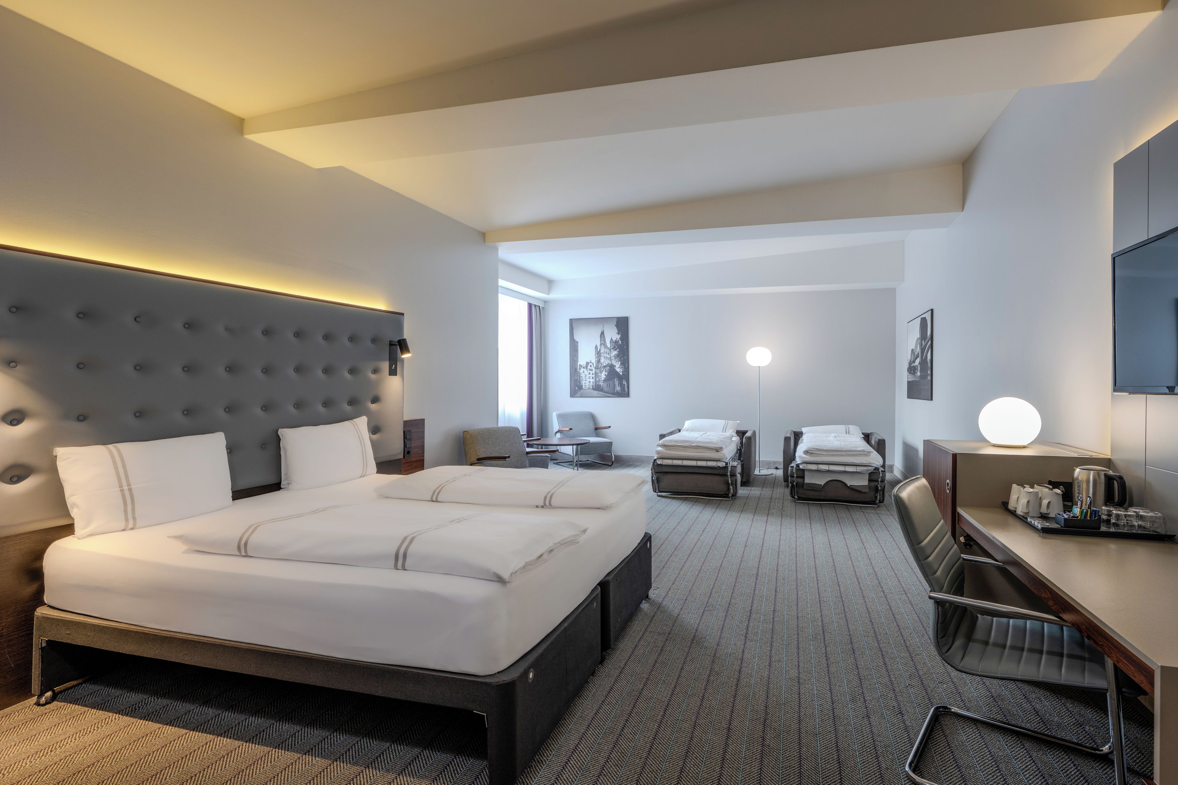 Une chambre d’hôtel avec un grand lit, un bureau, une chaise, un téléviseur à écran plat et une fenêtre avec des rideaux.