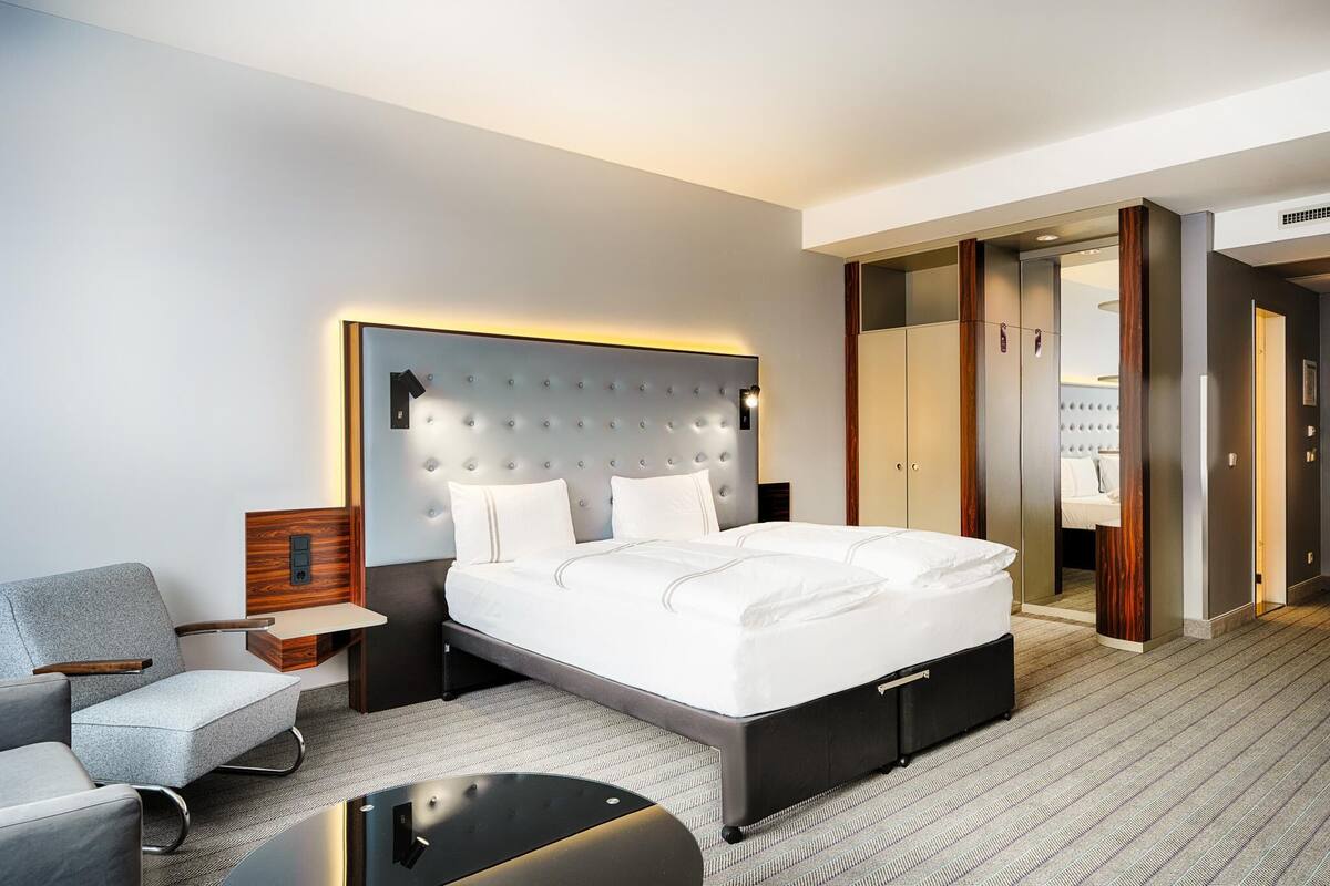 A modern hotel room with a large bed, a seating area, and a walk-in closet.