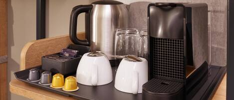 A kitchen counter with a coffee maker, kettle, toaster, and various coffee pods.