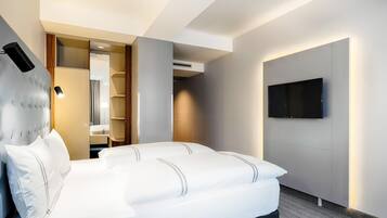 Una habitación de hotel moderna con una cama grande, un televisor de pantalla plana montado en la pared y un vestidor.