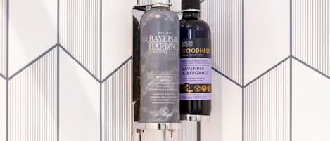 Duas embalagens de Baylis & Harding Elements numa parede com padrão geométrico.