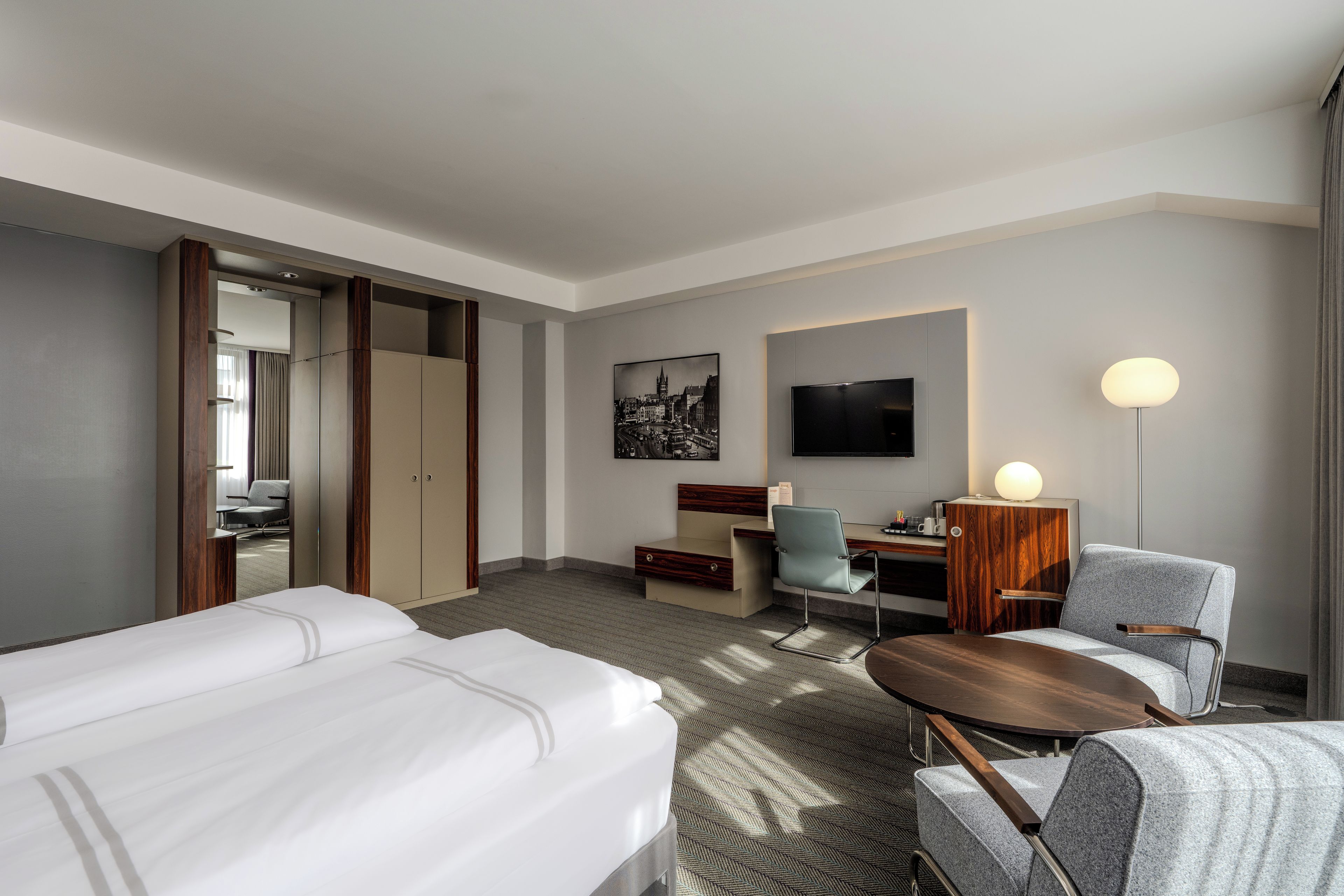 A hotel room with a bed, a desk, a chair, a television, and a lamp.