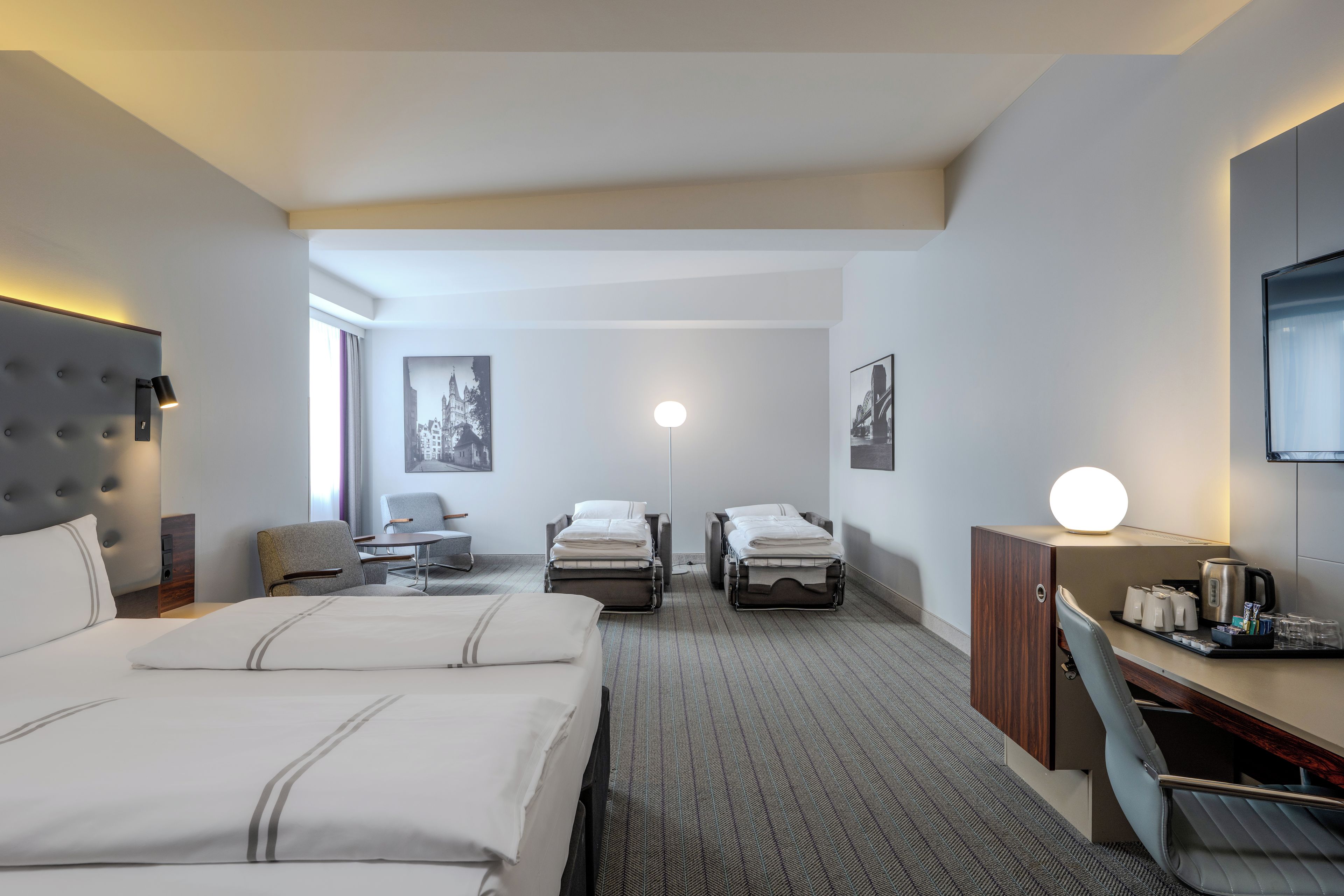 A hotel room with a large bed, a desk with a chair, a small table, and a sofa.