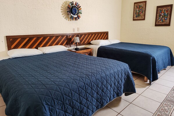A hotel room with two beds, a wooden headboard, a nightstand, a wall clock, and two framed artworks. - The Halfwaiy Inn (Guerrero Negro)