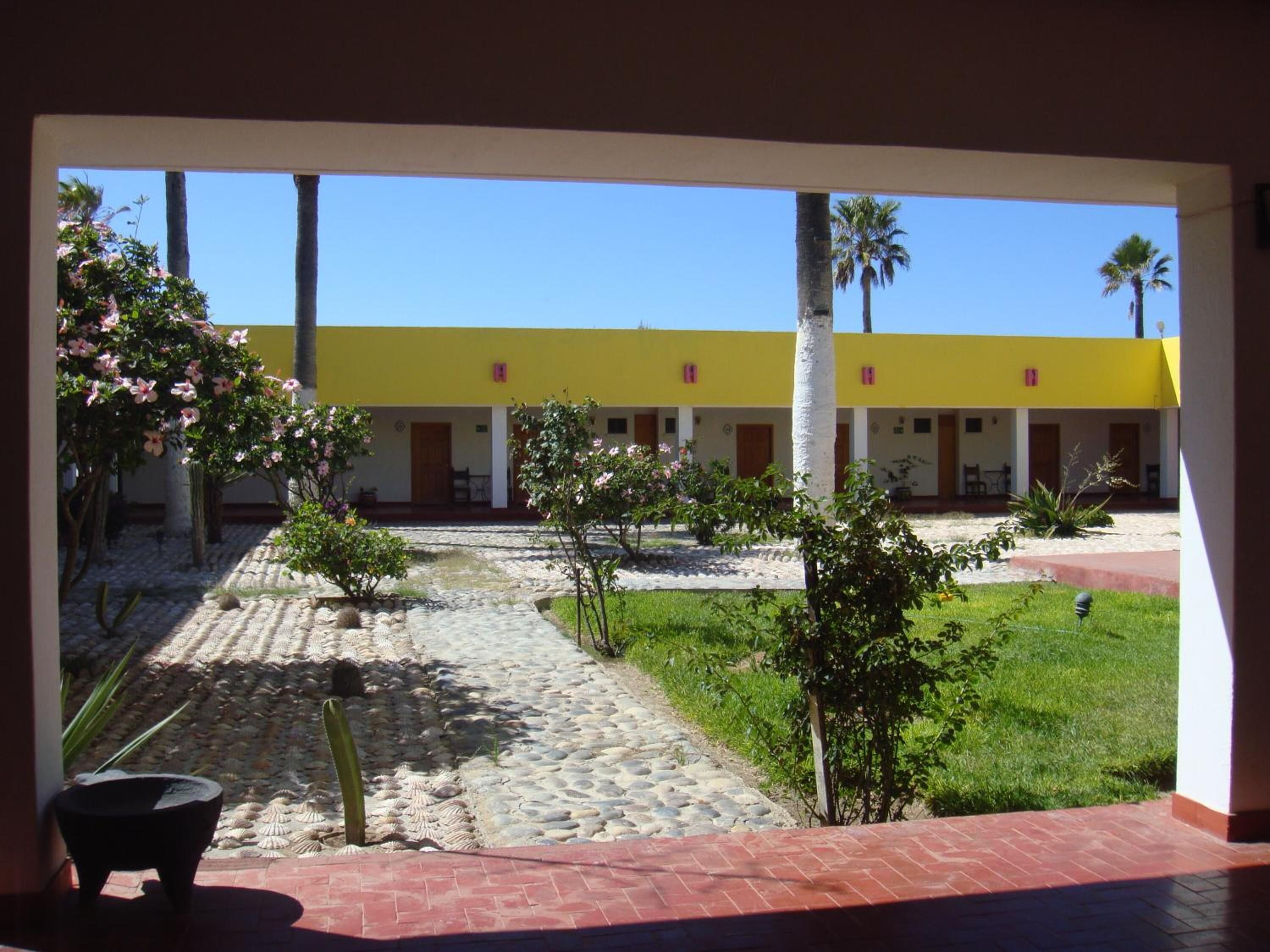 A courtyard with a yellow building, palm trees, and a stone pathway.