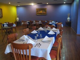 Un restaurante con varias mesas dispuestas para comer, sillas de madera y mantel azul.