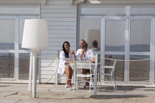Una pareja sentada a una mesa con vistas a la playa, una lámpara blanca y una barandilla.