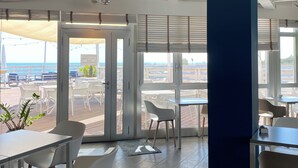 A modern interior with a view of the sea, featuring a dining area with tables and chairs, large windows, and a blue accent wall. - Terme Beach Resort (Ravenna)