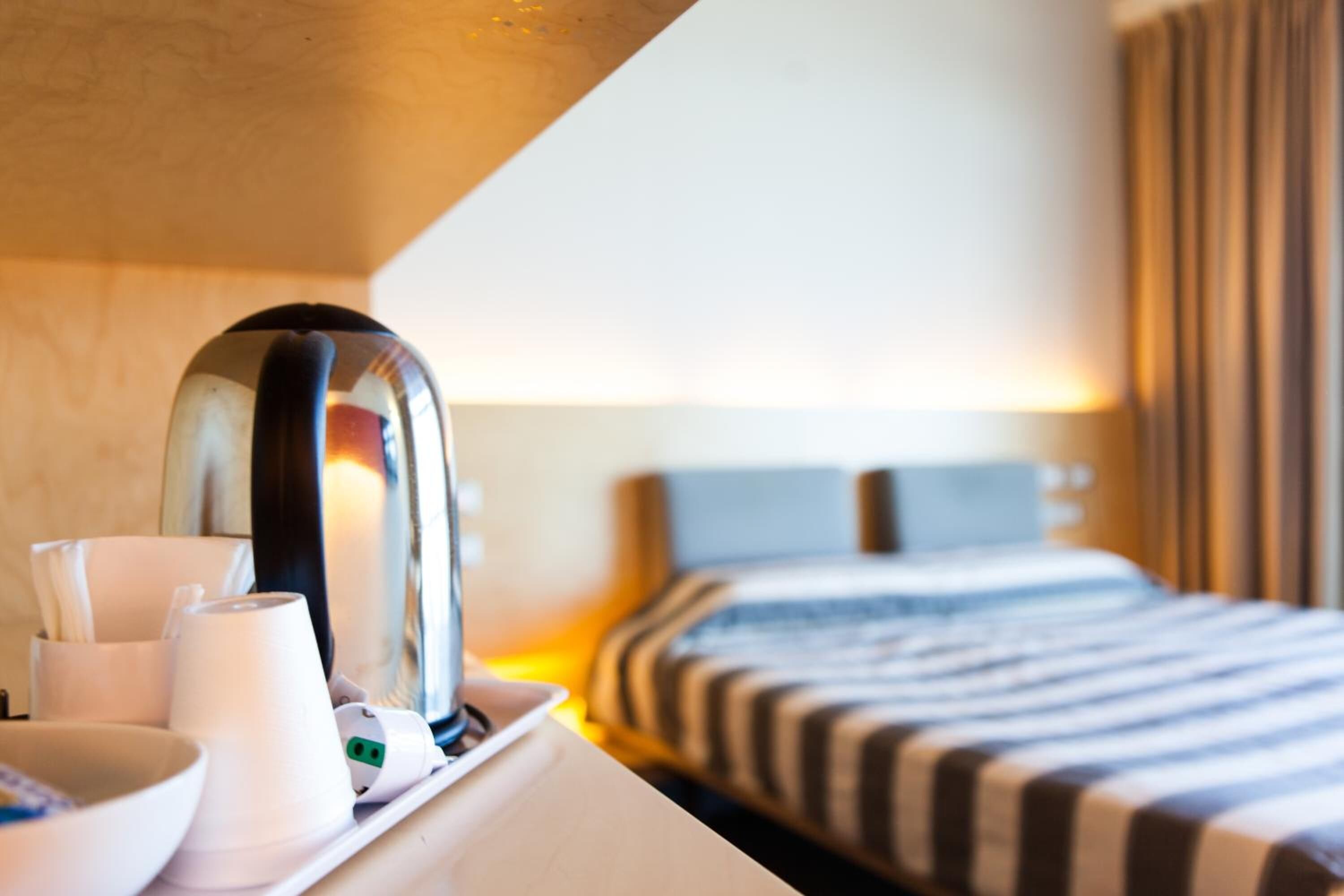 Una camera d'albergo con un letto, un comodino e un bollitore.