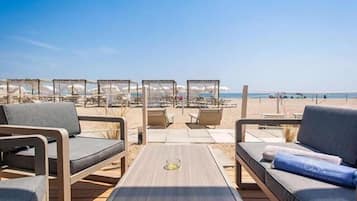 Een privéstrand, ligstoelen aan het strand, parasols, een strandbar