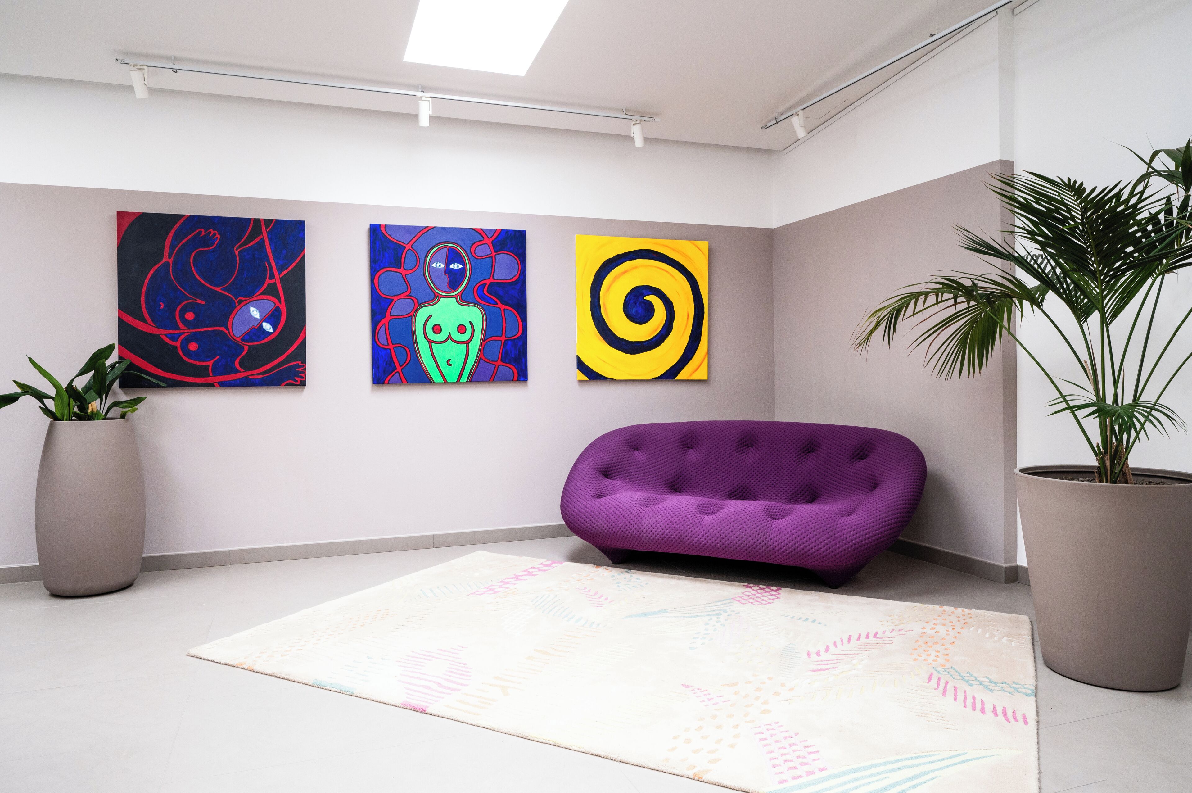 Una habitación moderna con un sofá púrpura, tres cuadros abstractos en la pared y dos plantas en macetas.