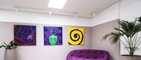 Una habitación moderna con un sofá púrpura, tres cuadros abstractos en la pared y dos plantas en macetas.