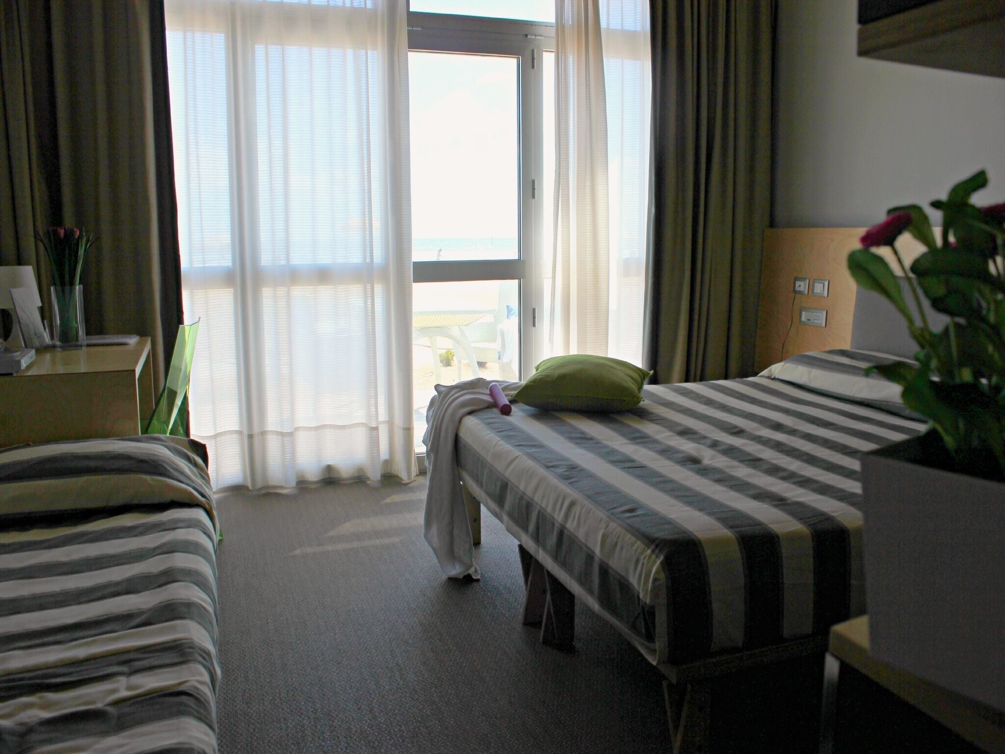 A hotel room with two beds, a desk, and a view of the outdoors.