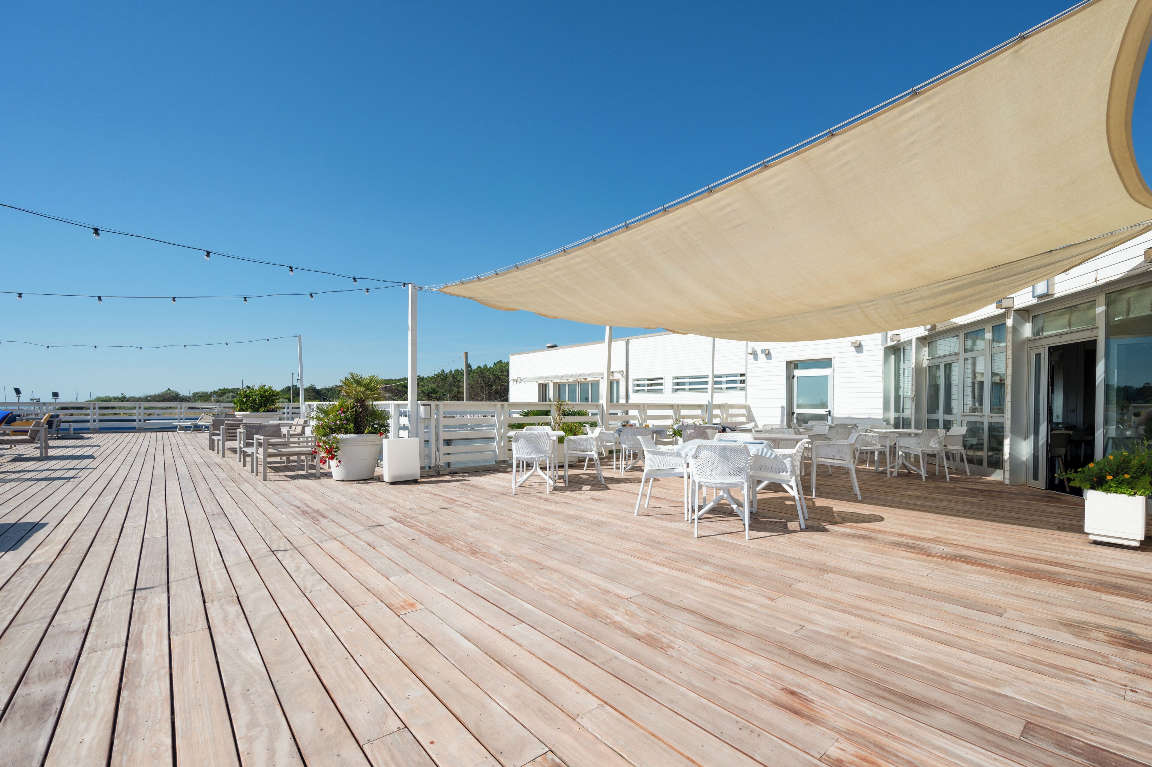 A wooden deck with outdoor seating, a large canopy, and a building with large windows.