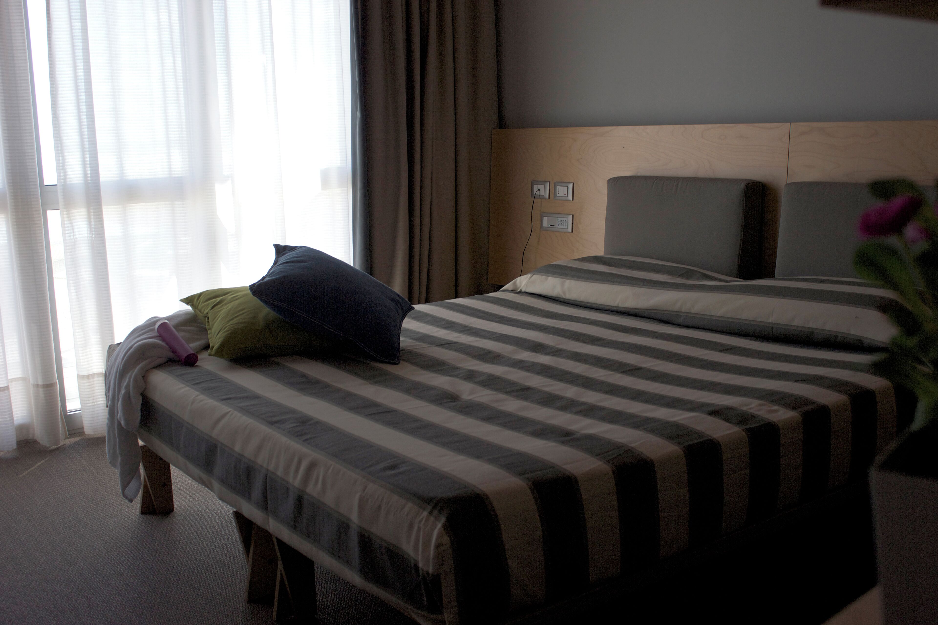 A hotel room with a bed, a headboard, and a window with curtains.
