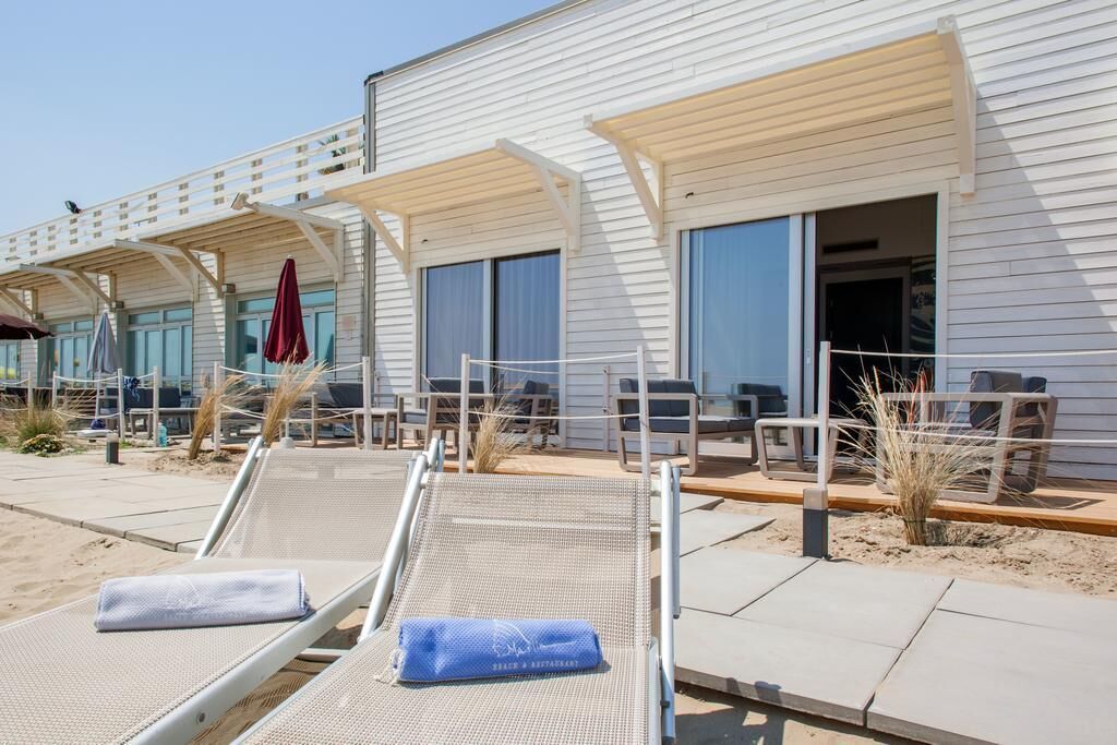 Ein Hotel direkt am Strand mit Liegestühlen im Freien, einer überdachten Terrasse und einem Sandweg.