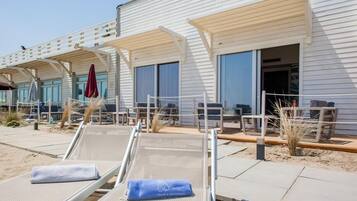 Ein Hotel direkt am Strand mit Liegestühlen im Freien, einer überdachten Terrasse und einem Sandweg.